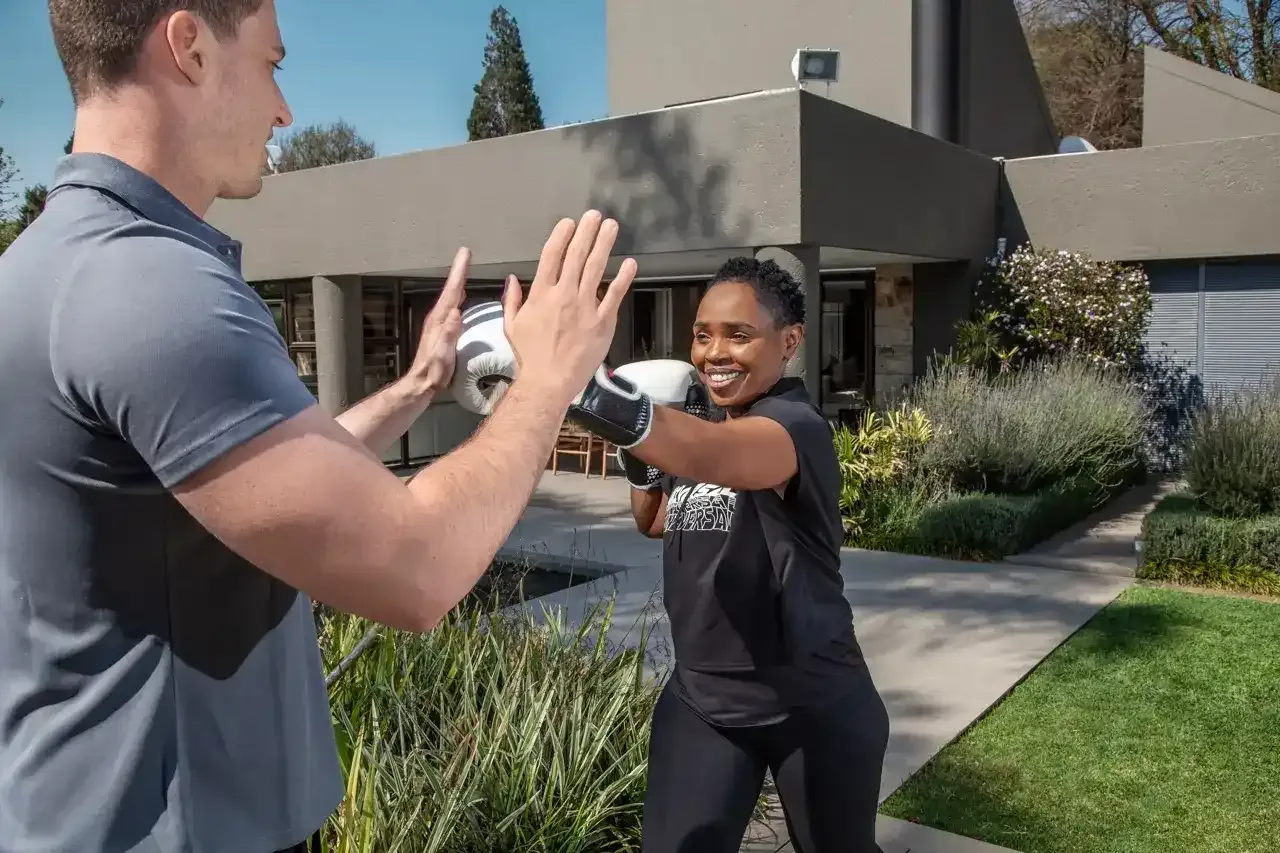 Client landing a punch into her trainer's open palm during a garden boxing session