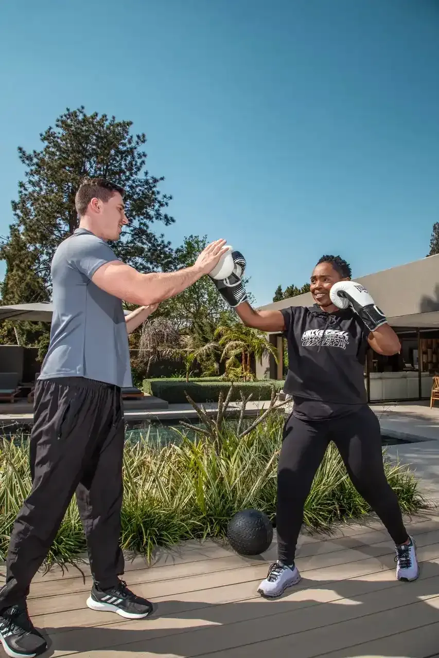 Full length view of a boxing client punching into a trainer's palm on a poolside deck