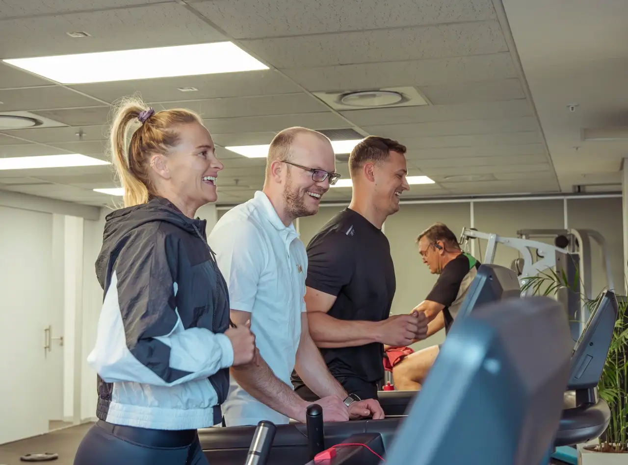Two clients and their trainer smiling side by side on treadmills in an office gym