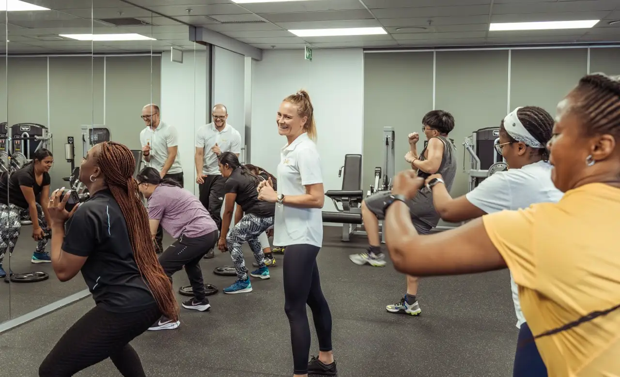 Female trainer smiling at the camera while leading a team workout in a corporate gym