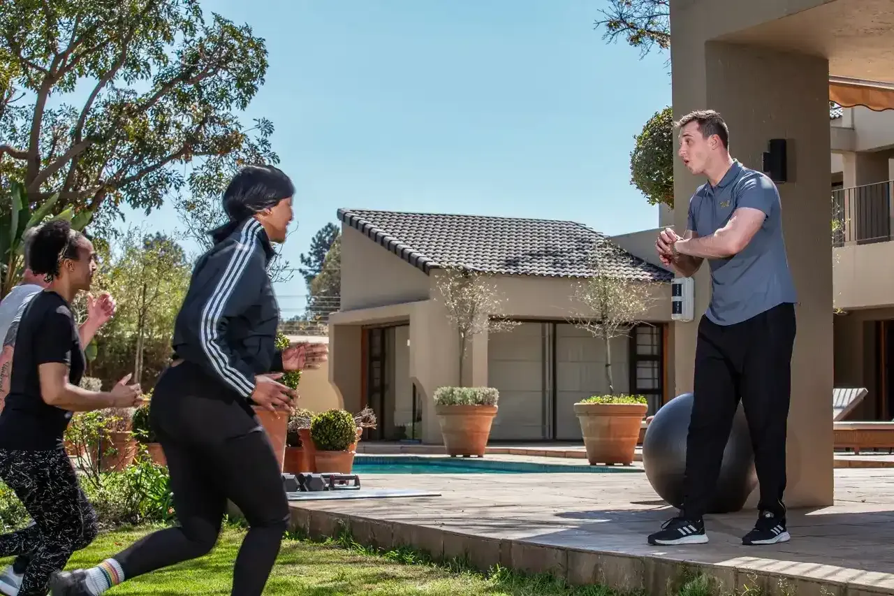Trainer cheering on three clients sprinting across a lawn beside a pool
