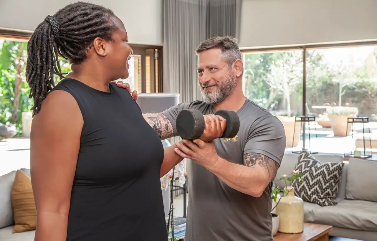 Trainer guiding a client through a dumbbell bicep curl in a sunlit living room