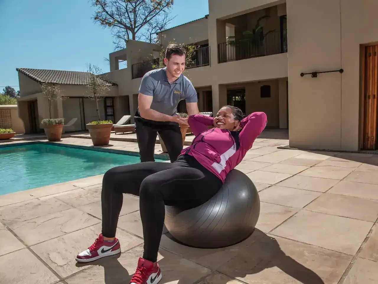 Trainer guiding a client through crunches on a stability ball beside a home swimming pool